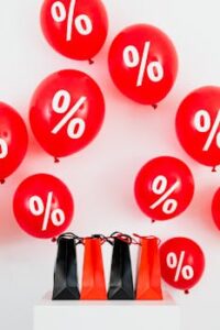Red and black shopping bags on a white background with red balloons featuring percentage symbols, ideal for sales.